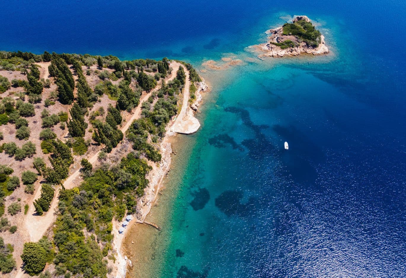 Aerial view of a lush coastline and small island surrounded by clear turquoise waters with a single boat.