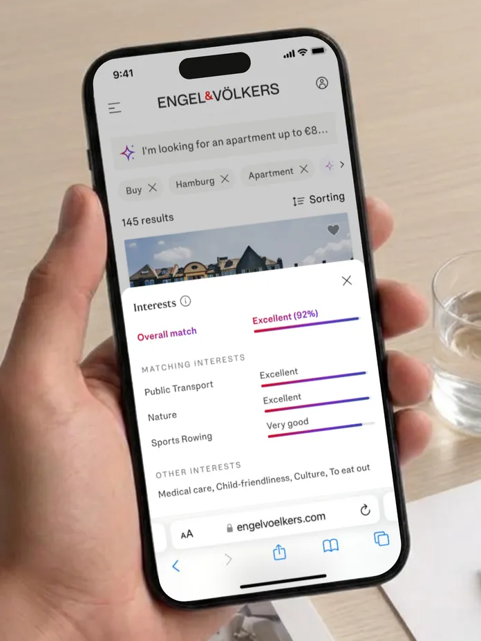 Hand holding a smartphone showing the Engel & Völkers website with AI Search and Interests overlay AI-generated image