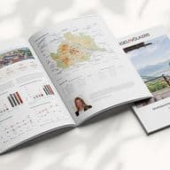 Open magazines displaying charts, graphs, and a map, alongside a closed magazine with a landscape cover, on a light surface.