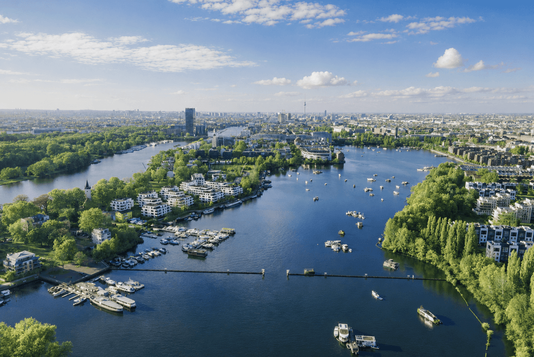 Aerial view of a river with marinas, boats and green tree-lined residential islands leading to a distant city skyline