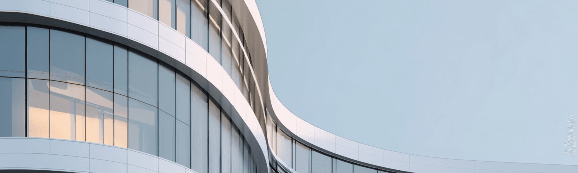 Curved modern glass office building with white horizontal bands and one warm-lit window against pale blue sky