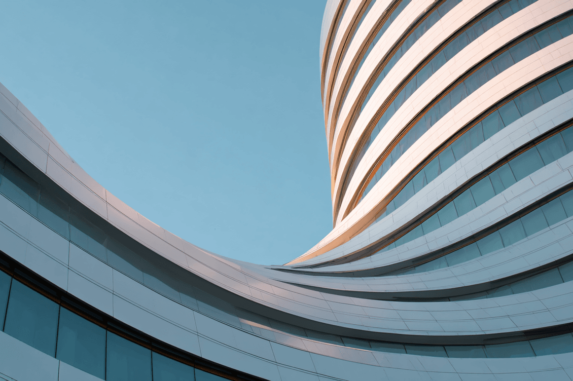 Modern building with smooth, wavy white facade and glass windows, set against a clear blue sky.