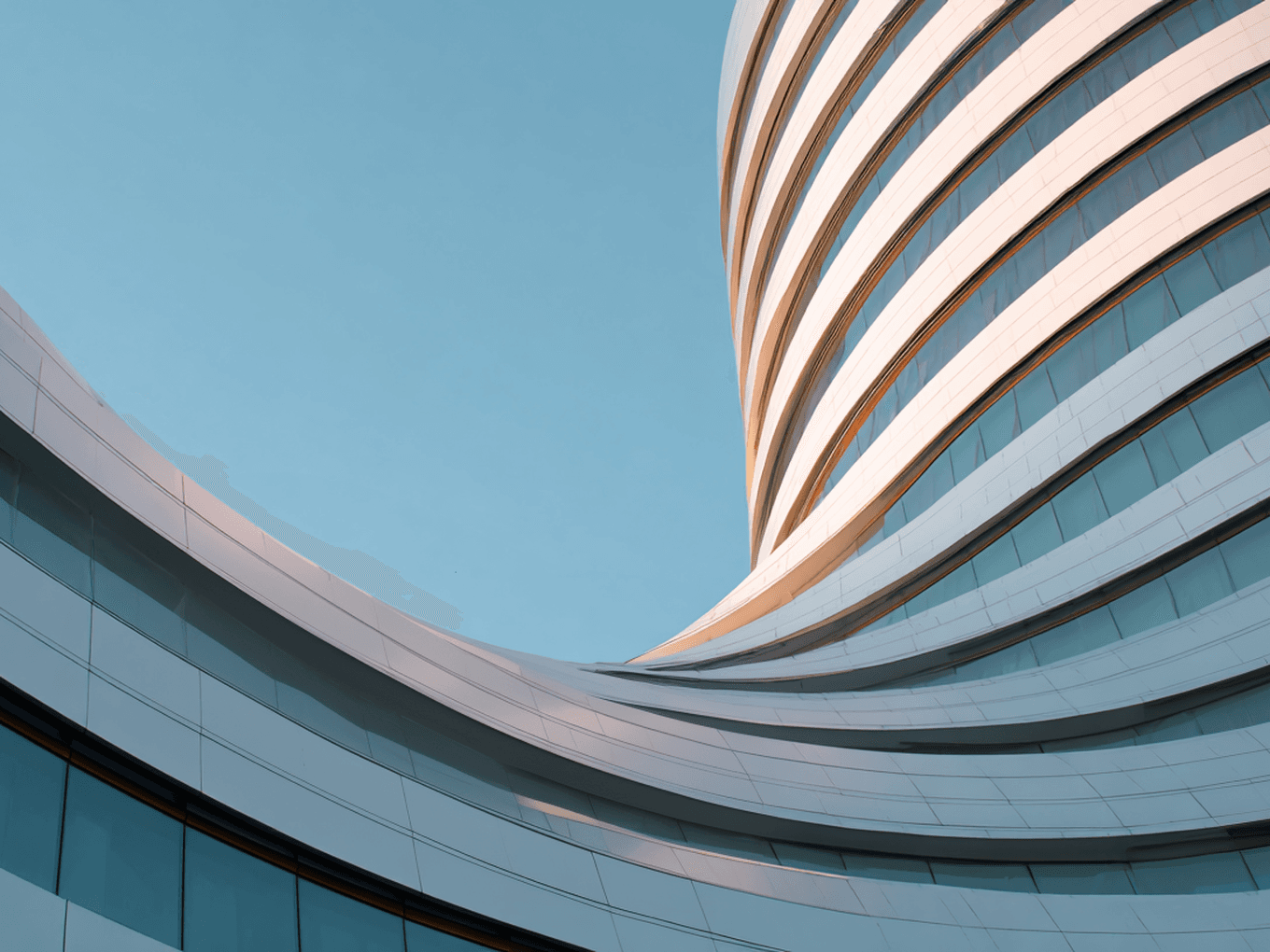 Curved modern building with sleek white and glass exterior against a clear blue sky.
