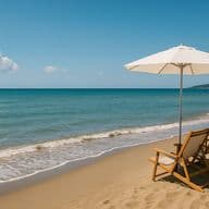 Zwei hölzerne Liegestühle unter einem weißen Sonnenschirm an einem Sandstrand, mit Blick auf ein ruhiges Meer und einen strahlend blauen Himmel.