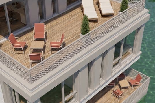 Modernes, mehrstöckiges Waterfront-Gebäude mit Holzterrassen, Lounge-Sesseln, Topfpflanzen und einer Solaranlage auf dem Dach über grünlichem Wasser.