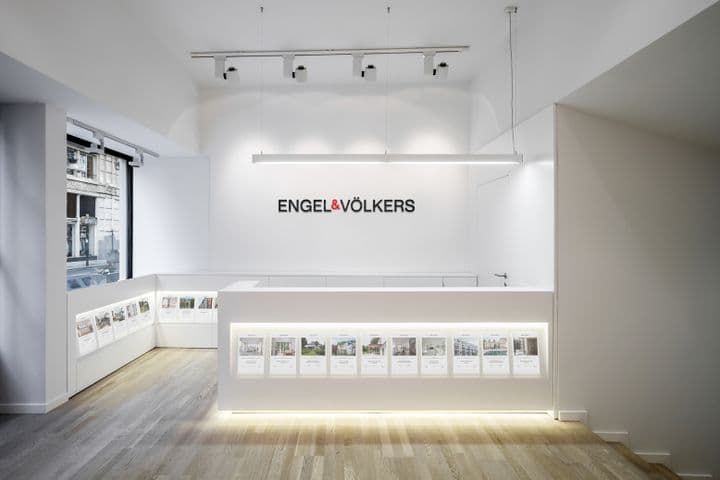 Helles, modernes Engel & Völkers Büro mit weißen Wänden, hellen Holzböden und einem eleganten Empfangstresen mit Immobilienangeboten.