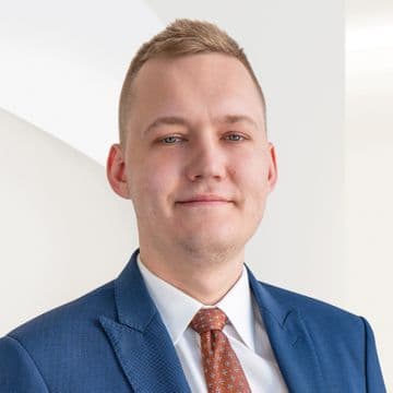 Portrait of a man wearing a blue suit, white shirt, and tie, facing the camera. The light background features the Engel & Völkers logo.