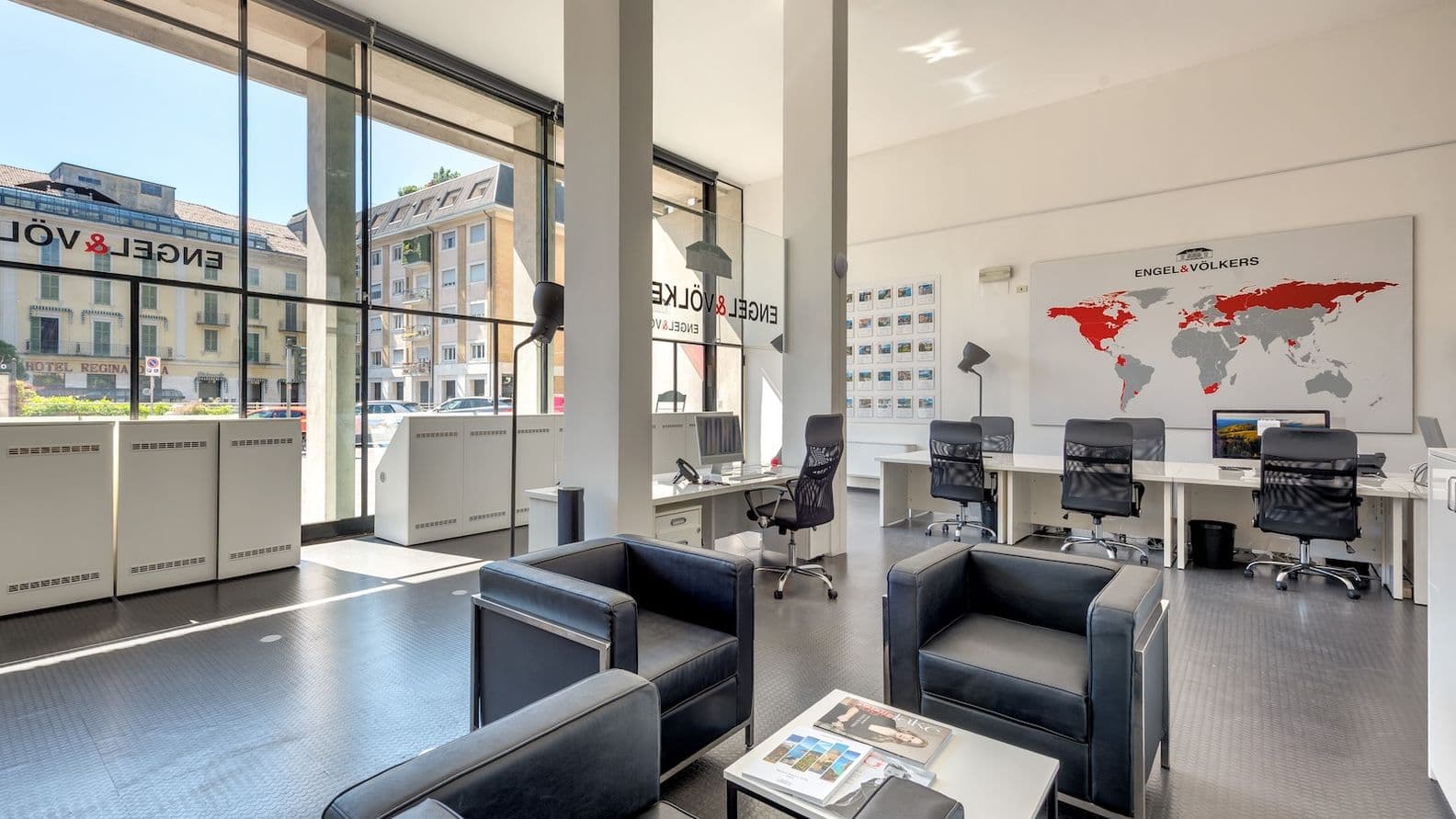 Bright modern office of Lake Como lobby with black leather seating, glass walls, desks and chairs, and a world map on the wall.