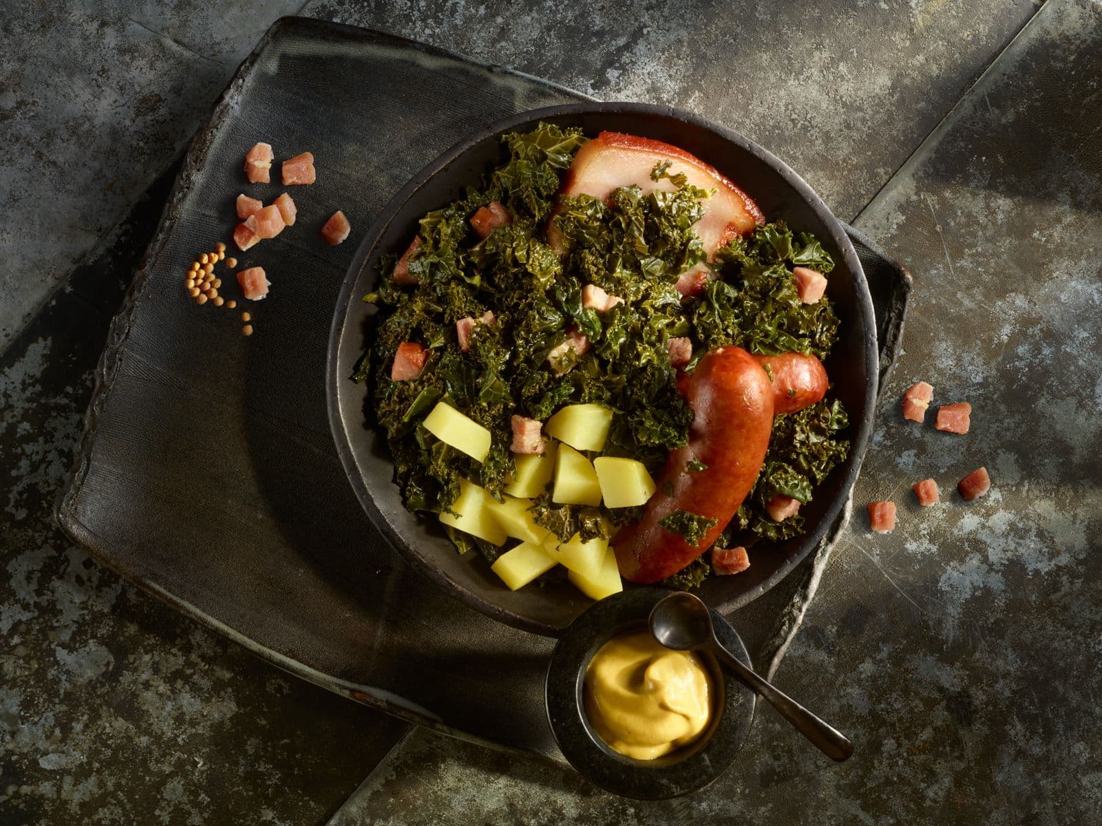 Traditionelles Grünkohlgericht mit Kasseler, Wurst, Kartoffeln und Senf auf rustikalem Geschirr - ein festliches Essen aus Norddeutschland