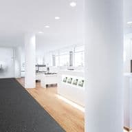 Modern real estate office interior with sleek white desks, computers, glossy reception desk, and a black couch on a carpeted floor.