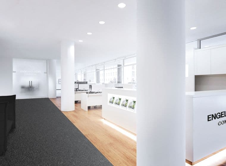 Modern real estate office interior with sleek white desks, computers, glossy reception desk, and a black couch on a carpeted floor.
