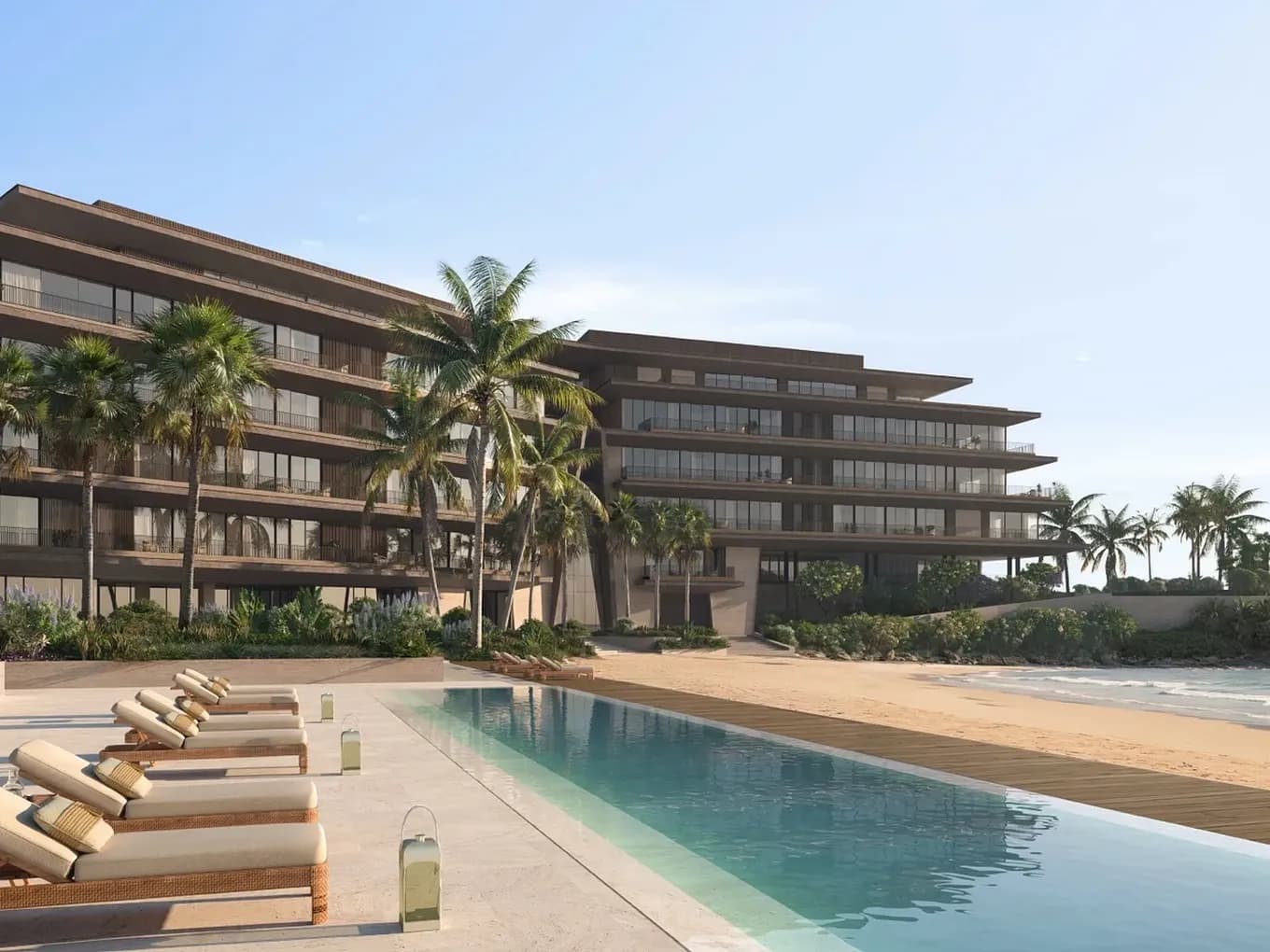 Beachfront resort with modern multi-story building, palm trees, and lounge chairs beside a long reflecting pool, overlooking the ocean.