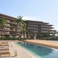 Beachfront resort with modern multi-story building, palm trees, and lounge chairs beside a long reflecting pool, overlooking the ocean.