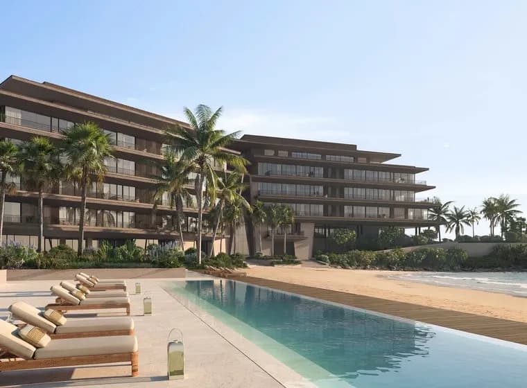 Beachfront resort with modern multi-story building, palm trees, and lounge chairs beside a long reflecting pool, overlooking the ocean.