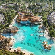Aerial view of a luxurious resort with turquoise lagoon, sandy beaches, modern architecture, and surrounding greenery and palm trees.