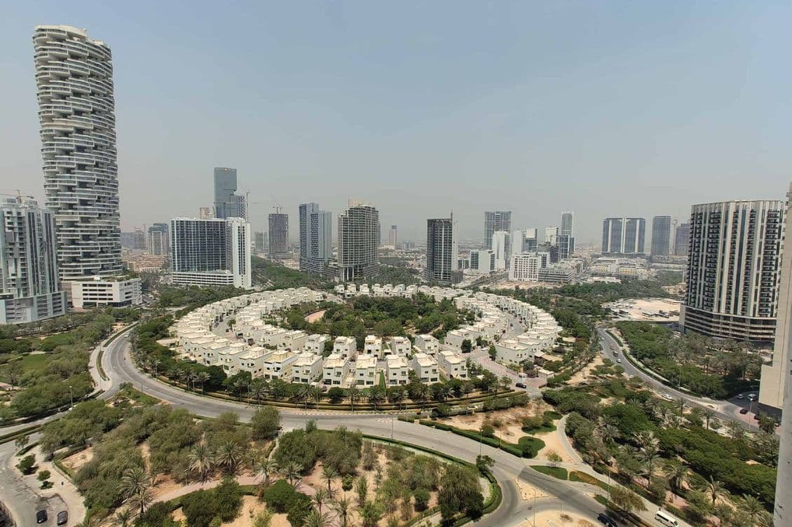 Aerial view of a cityscape with circular residential complex, surrounded by greenery and tall buildings under a hazy sky.