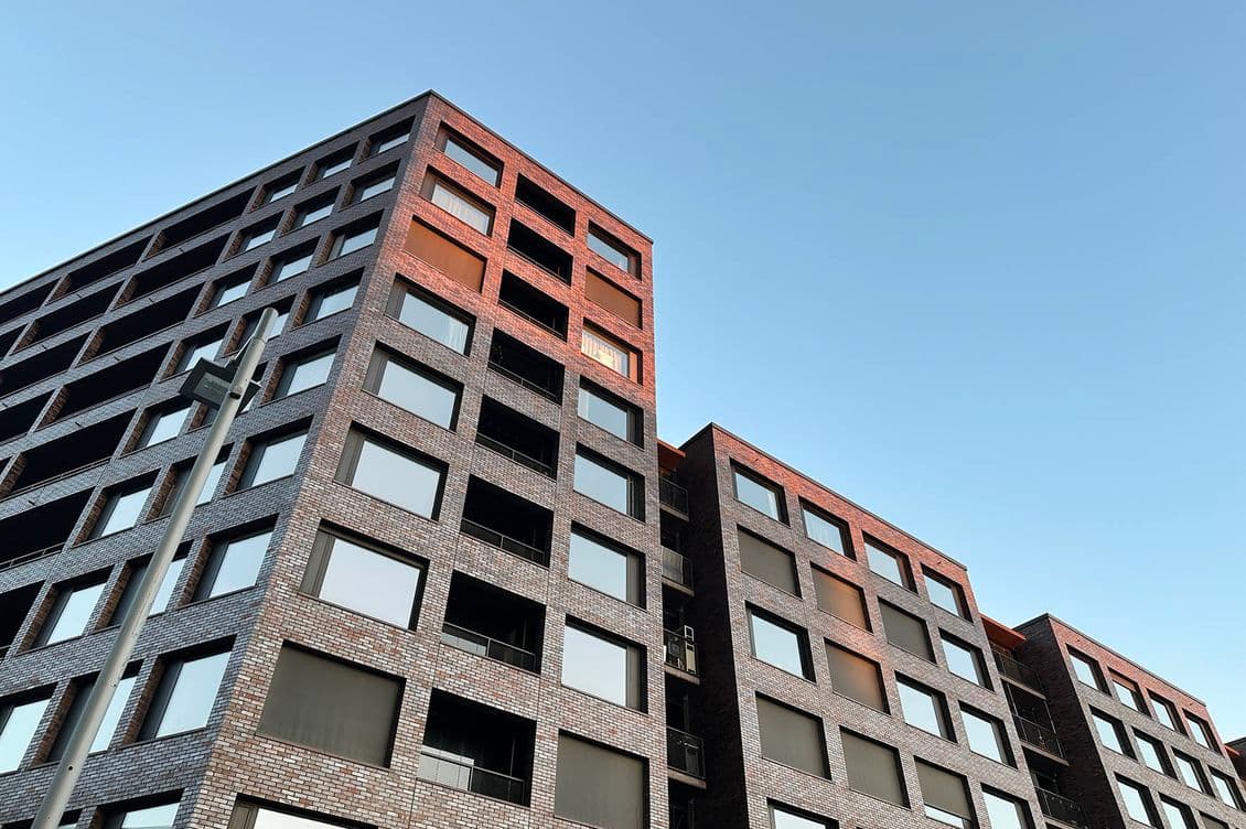 Niedrige Perspektive auf moderne Wohnhäuser aus Backstein und Glas vor einem strahlend blauen Himmel.