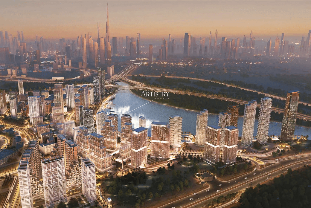 Aerial view of a cityscape at sunset, featuring illuminated skyscrapers, a body of water, and a distant skyline with a tall tower.