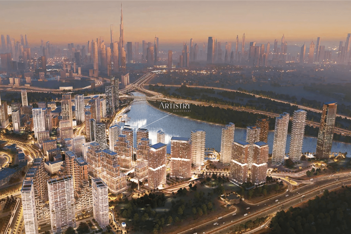 Aerial view of a cityscape at sunset, featuring illuminated skyscrapers, a body of water, and a distant skyline with a tall tower.