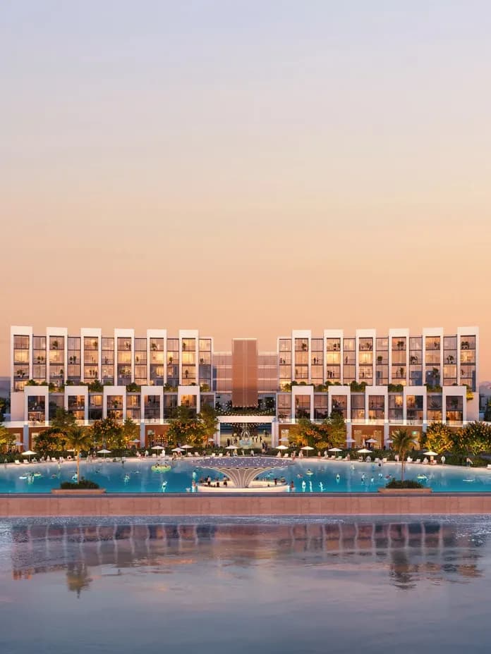 Modern beachfront resort at sunset, featuring symmetrical architecture, lush landscaping, and a tranquil pool reflecting the sky.