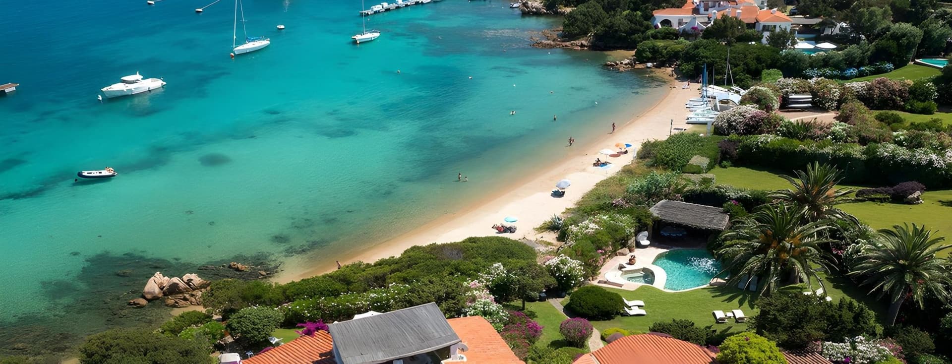 Aerial view of a scenic coastal village with turquoise waters, white sand beach, yachts, and lush greenery surrounding charming red-roofed houses.