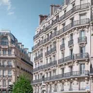Elegant Parisian buildings with ornate balconies under a clear blue sky, surrounded by lush green trees.