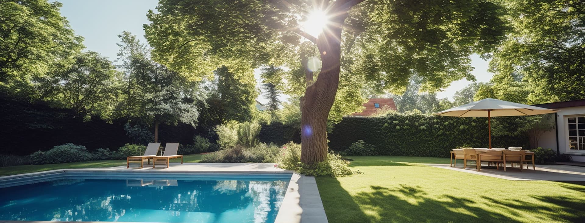 Sunlit backyard with a pool, lounge chairs, a large tree, and a patio set under an umbrella, surrounded by lush greenery.