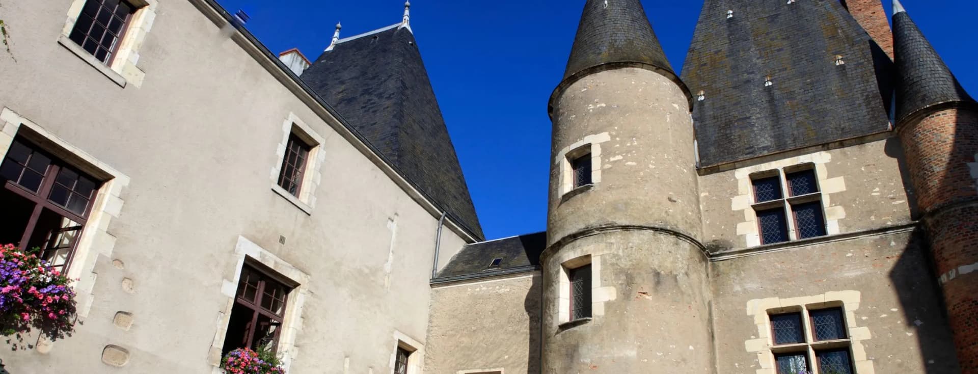 Historic stone building with conical towers and flower-adorned windows under a clear blue sky.