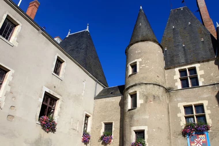 Historic stone building with conical towers and flower-adorned windows under a clear blue sky.