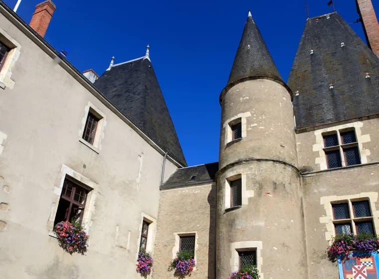 Historic stone building with conical towers and flower-adorned windows under a clear blue sky.