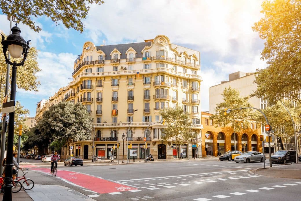Eine malerische Straße mit einem historischen Gebäude, Radweg, Straßenlaterne, Radfahrer und Taxis unter sonnigem Himmel mit vereinzelten Wolken.