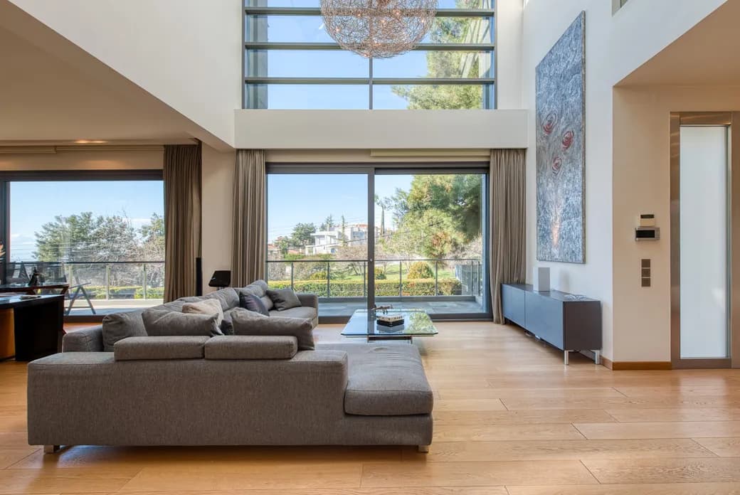 Bright modern living room with a grey sectional, glass coffee table, large windows and balcony view, a spherical chandelier, and abstract wall art.