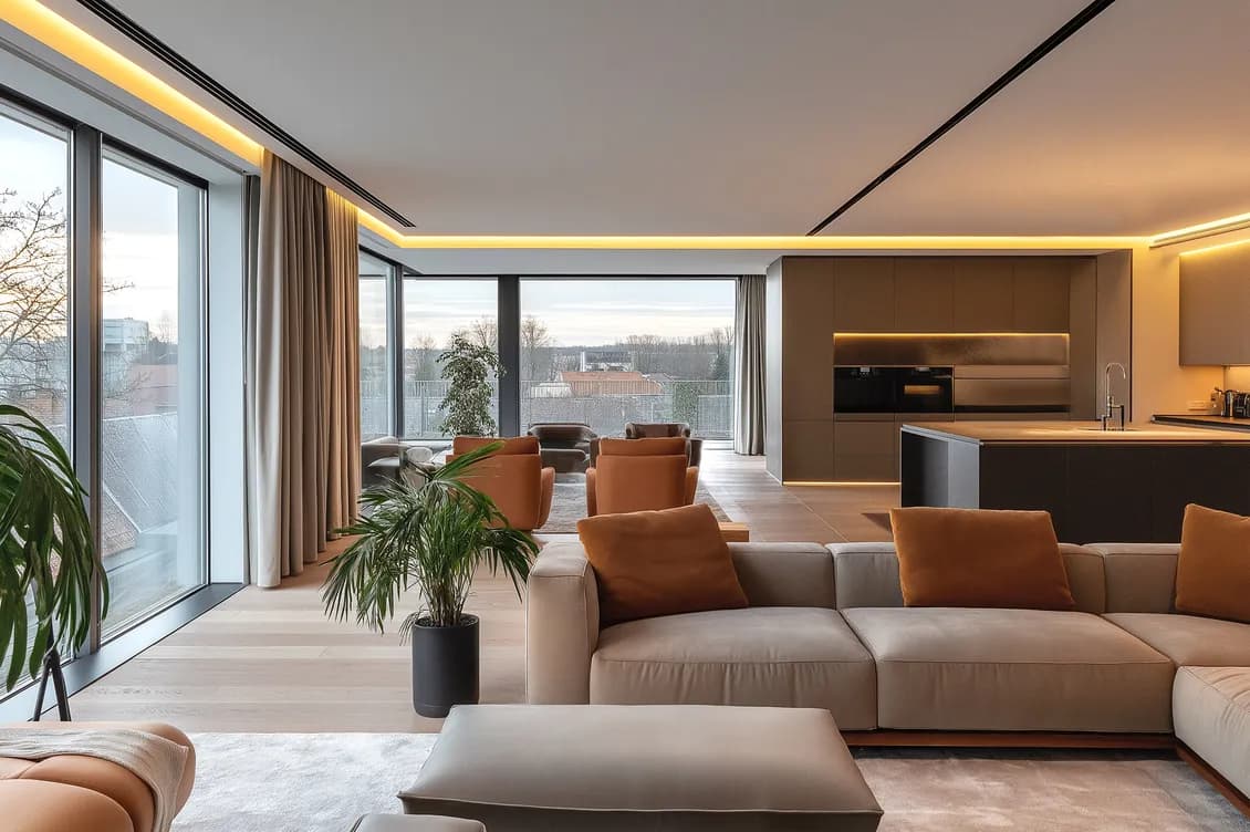 Lussuoso attico con vetrate a tutta altezza, divano ad L grigio, poltrone in pelle marrone chiaro e cucina a vista. L'ambiente è arricchito da piante da interno e illuminato da calde luci a LED a soffitto, mostrando un design contemporaneo dai toni neutrali e una grande luminosità naturale. AI-generated image