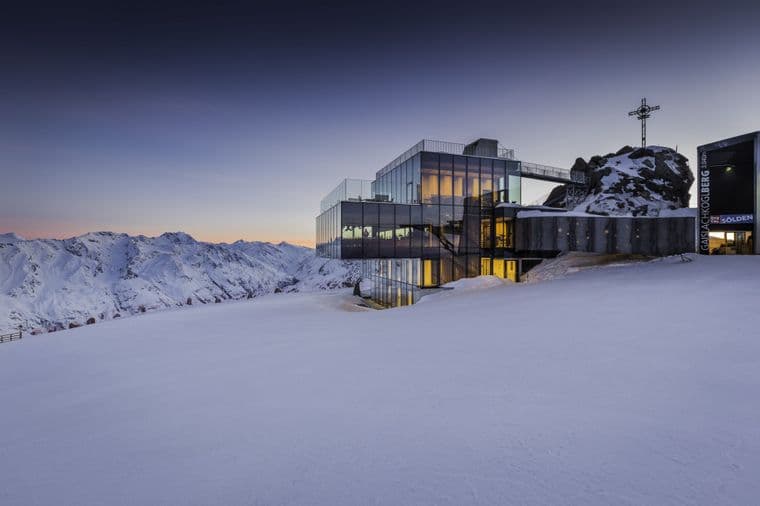 Modern glass building of the ICE Q Restaurant in Sölden on a snow-covered mountain peak with a breathtaking Alpine backdrop.