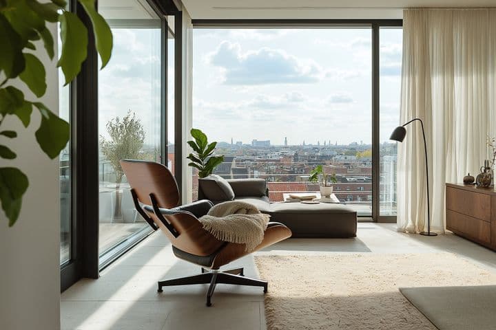 Moderní interiér penthousu s designovým odpočinkovým křeslem a přehozem, otočeným k proskleným oknům sahajícím od podlahy ke stropu s výhledem na městskou scenérii. Prostor doplňují pokojové rostliny, krémové závěsy a krémový koberec, čímž vzniká světlý, minimalistický čtecí koutek zalitý přirozeným světlem