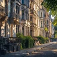 Row of elegant historic buildings with decorative balconies and classical architecture along a cobblestone street. The facade features ornate stonework and wrought iron railings, with lush greenery and tree shadows creating a peaceful urban scene in early morning light.