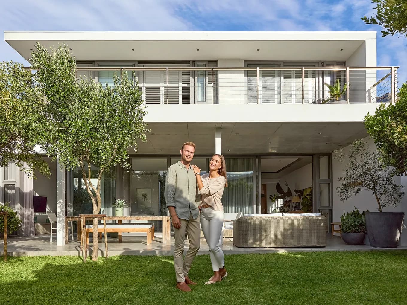 Happy couple in the garden of their financed property – a modern, two-story house with a balcony.
