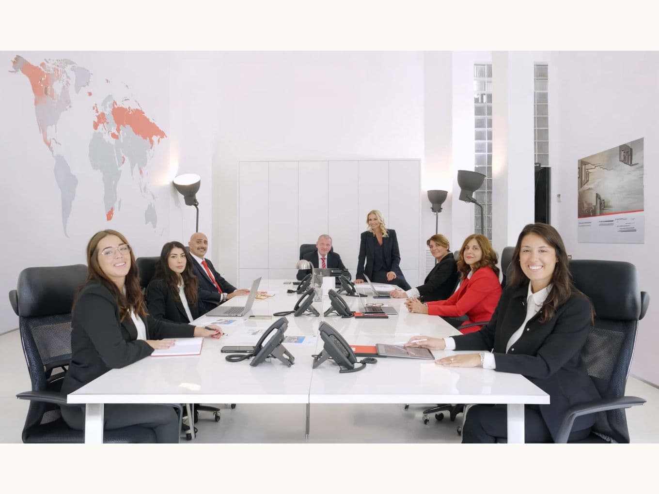 professionals about Lake Como Team sit around a white conference table in a bright office, with phones and a world map on the wall.