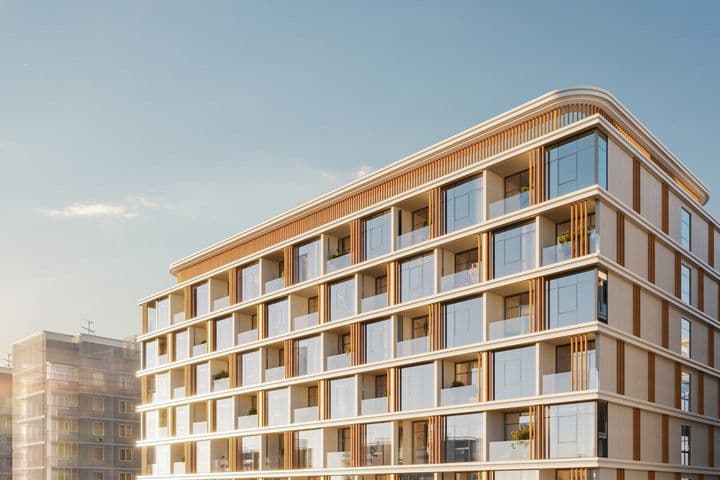 Modern building with glass balconies and brown accents under a clear blue sky, adjacent to other residential structures.
