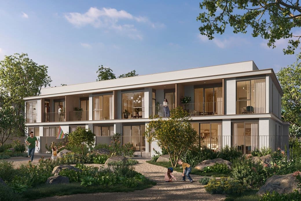 Modern two-story building with balconies, surrounded by lush greenery and a garden. People are enjoying the sunny day outdoors.