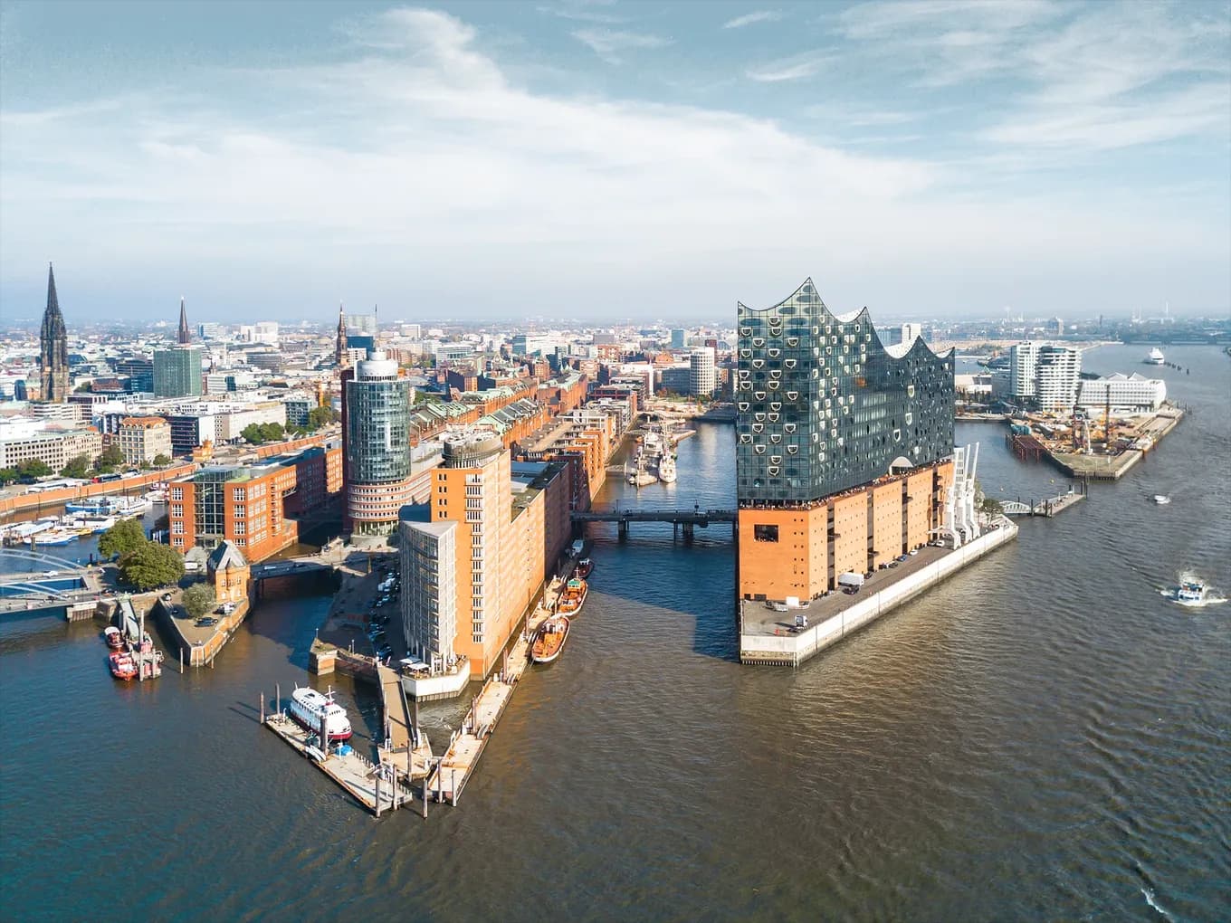 Aerial view of Hamburg’s HafenCity with the Elbphilharmonie at the forefront, surrounded by modern buildings, waterways, and ships – a landmark and popular tourist attraction in Hamburg.