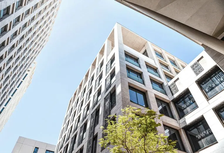 Blick von oben auf ein modernes Geschäftsgebäude mit geometrischer weißer Fassade, mit sich wiederholenden Fenstermustern, Glaselementen und einem jungen Baum im Vordergrund vor einem blauen Himmel