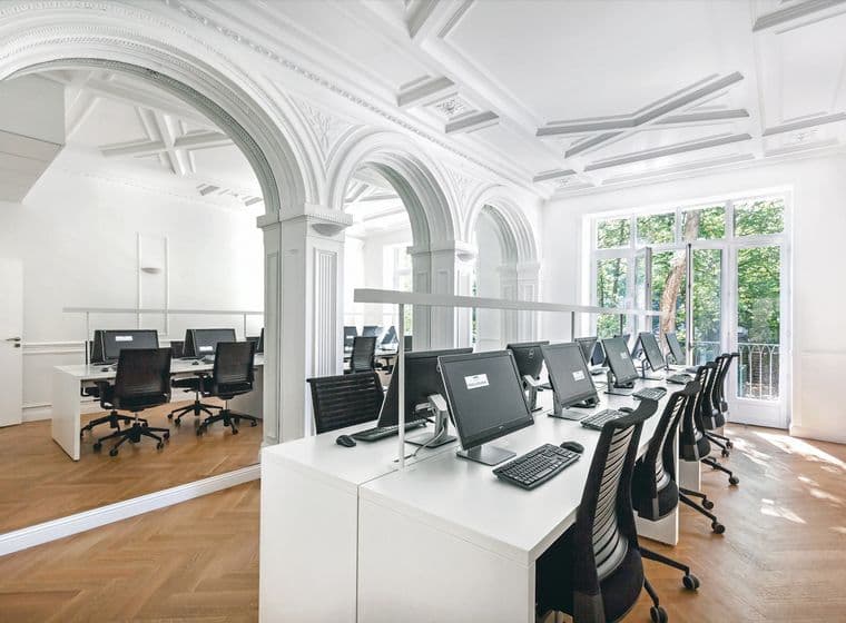 Bright, modern office space with rows of computers on white desks, large windows, and decorative arches.