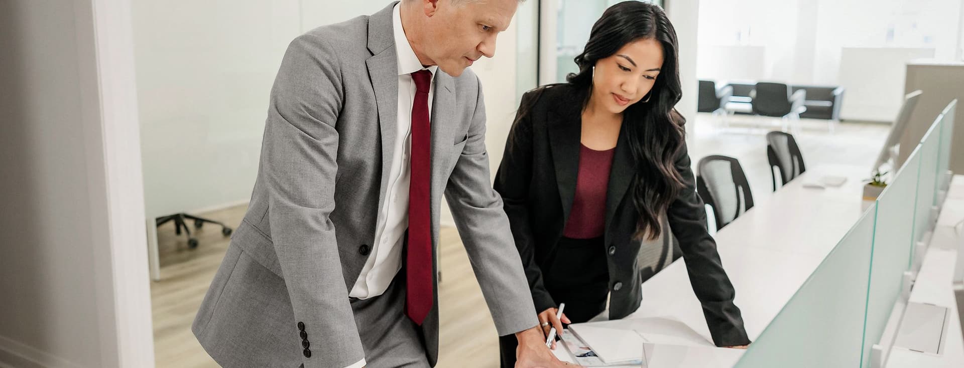 Dos agents immobiliaris, un home i una dona, revisen documents de propietat en un escriptori blanc en una oficina moderna i lluminosa.