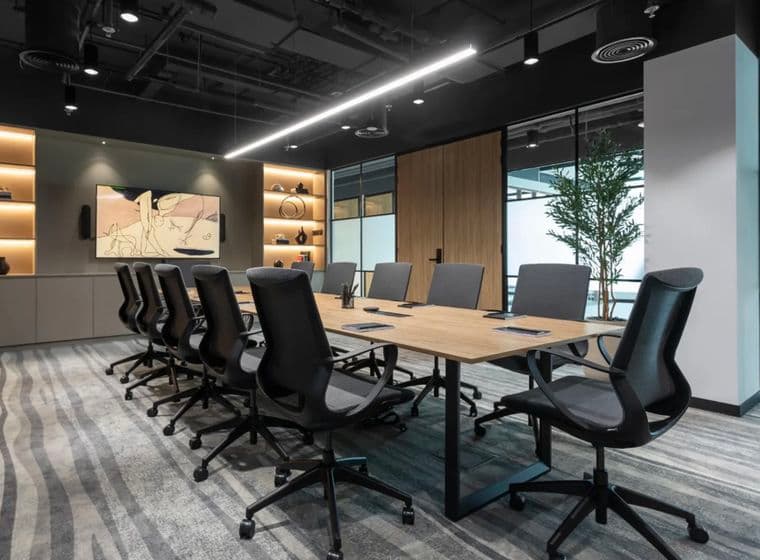 Modern conference room with a long wooden table, black swivel chairs, shelves with decor, and a large artwork on the wall.