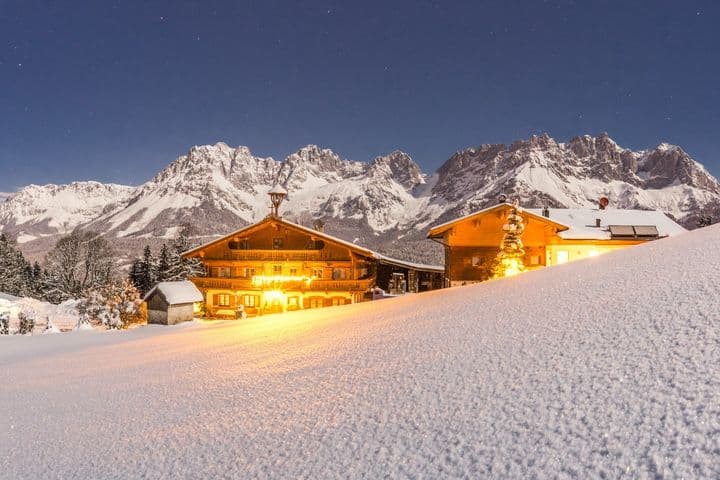 An illuminated chalet in a deeply snow-covered landscape against an impressive Alpine backdrop under a clear starry sky - a primary residence in Tyrol with a unique atmosphere.