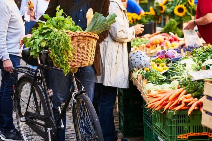 A bicycle with a basket full of fresh vegetables in front of a colorful market stall