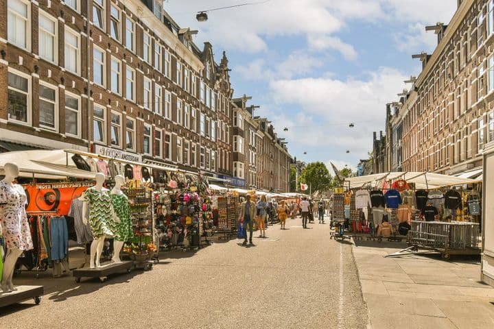 Street view of Albert Cuyp Market in Amsterdam, Netherlands. Vendors sell clothing and souvenirs from stalls. People walk along the street.