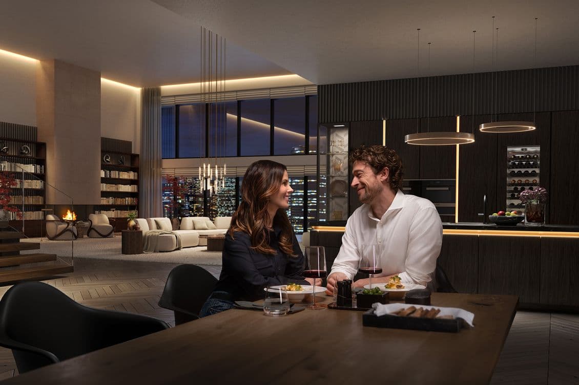 A couple enjoys a dinner in a luxurious modern apartment with a city view, ambient lighting, and elegant decor.