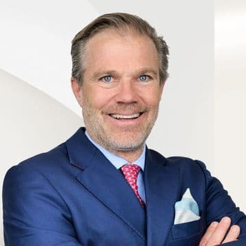Philipp Preuss in einem blauen Anzug mit roter Krawatte und Einstecktuch vor einem hellen Hintergrund.